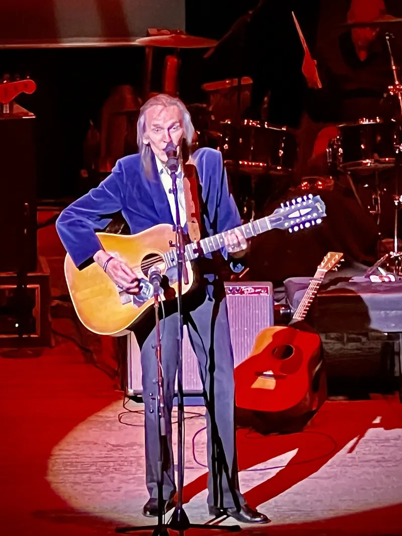 Gordon Lightfoot playing a twelve-string acoustic guitar under a red spotlight
