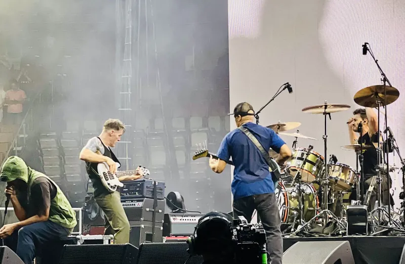 Rage Against the Machine on a smoky stadium stage, bassist and guitarist facing the drummer